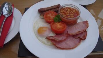 A breakfast plate with eggs, bacon, tomatoes, beans, and sausages.