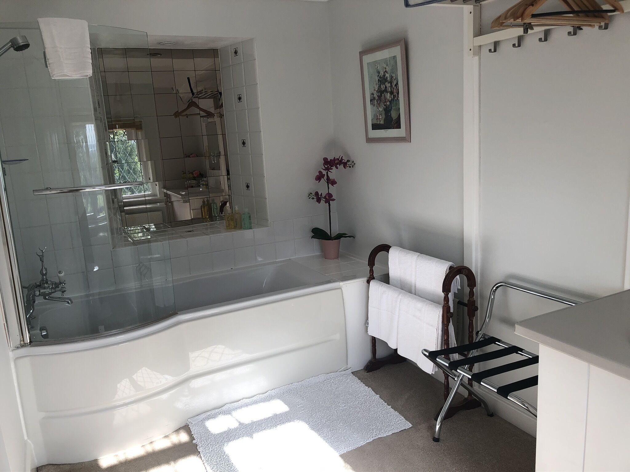 Un baño moderno con ducha envuelta en vidrio, una bañera blanca y una silla de madera con una toalla.