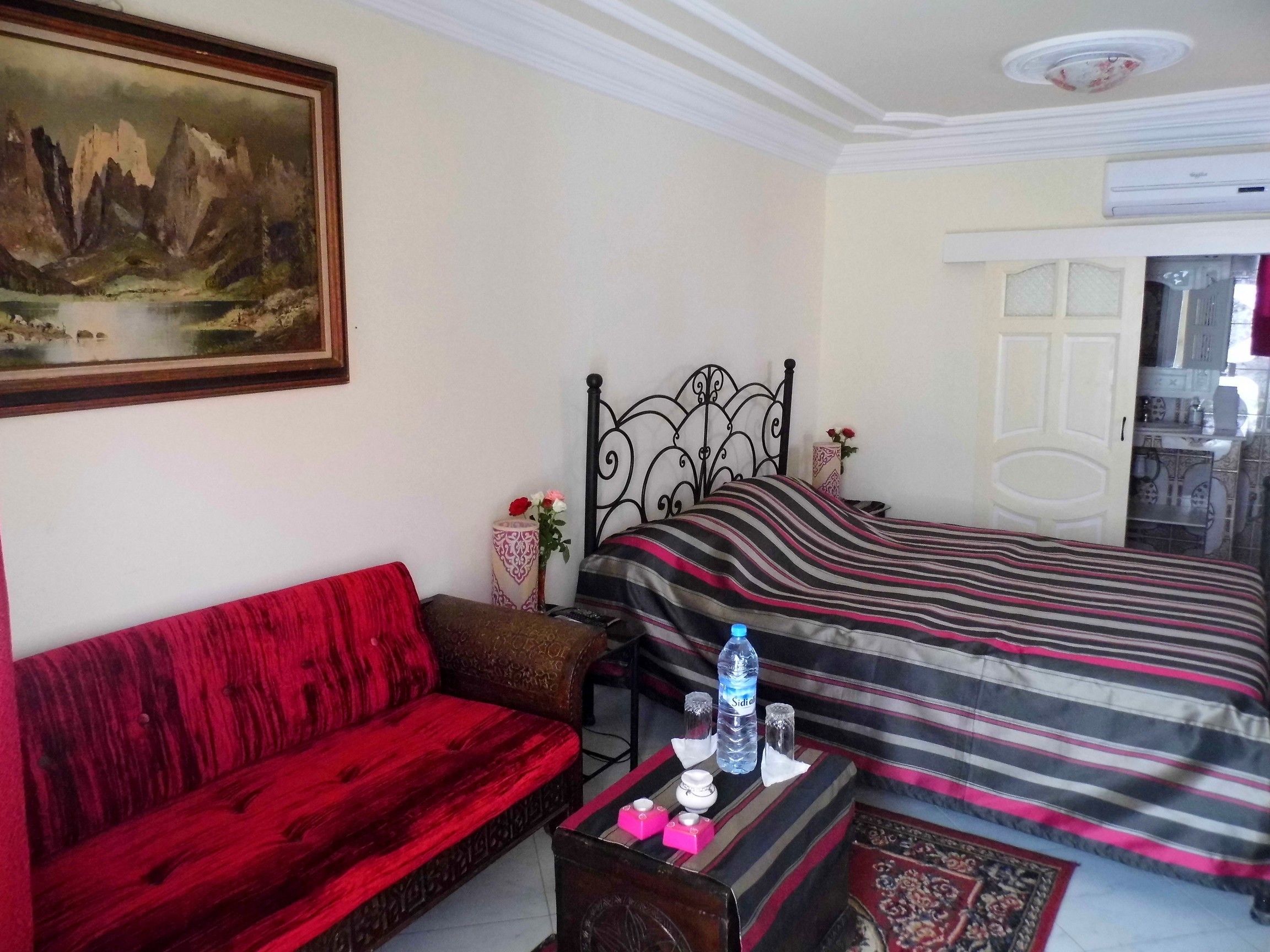Un dormitorio con una cama, un sofá rojo, un cuadro y un baño visible a través de una puerta abierta.