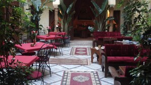 Une cour intérieure avec des tables et des chaises rouges, entourée de grandes plantes et dotée d’un sol carrelé.