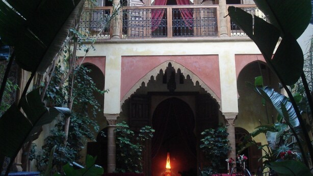 A courtyard with a central archway, a balcony with red curtains, and surrounding greenery. - Riad Marlinea (Salé)