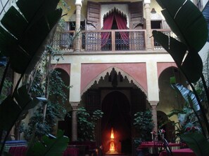 A courtyard with a central archway, a balcony with red curtains, and surrounding greenery. - Riad Marlinea (Salé)