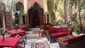 Une cour intérieure avec des tables et des chaises rouges, un canapé et un tapis décoratif.