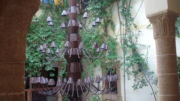 A wrought iron chandelier with multiple arms and hanging bells, set in an outdoor area with ivy-covered walls and stone columns.