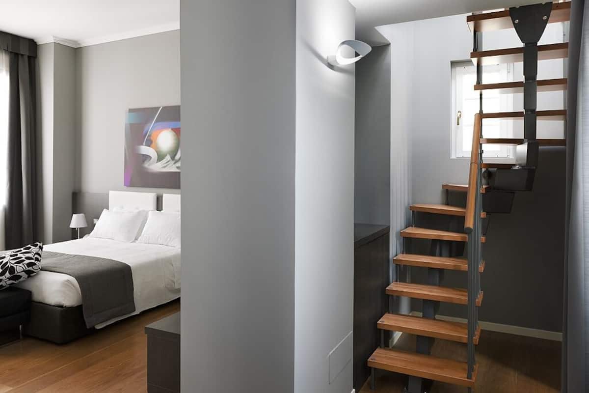 A modern bedroom with a bed, bedside table, and a wooden staircase.