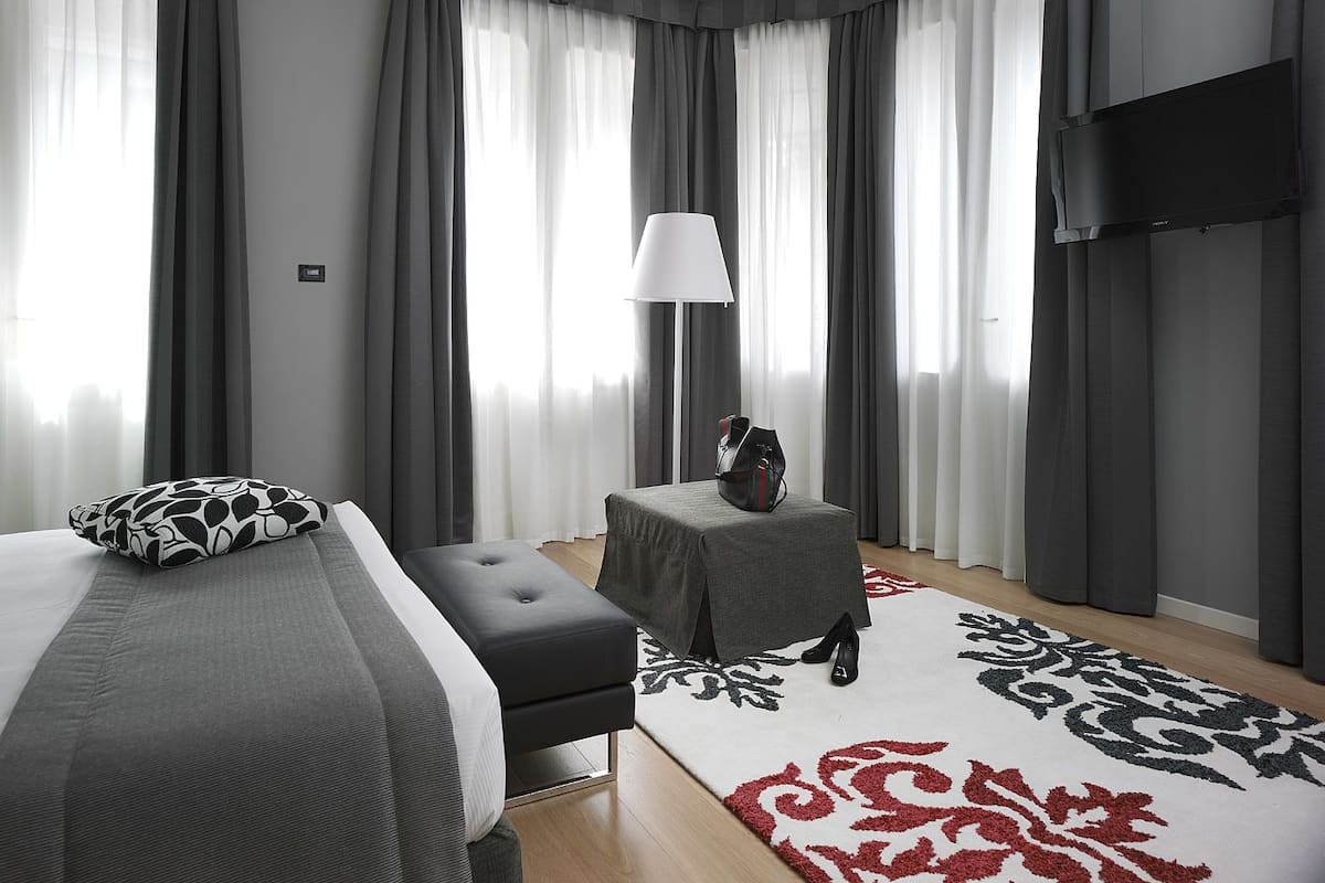 A modern hotel room with a large bed, a small table, a lamp, and a TV.