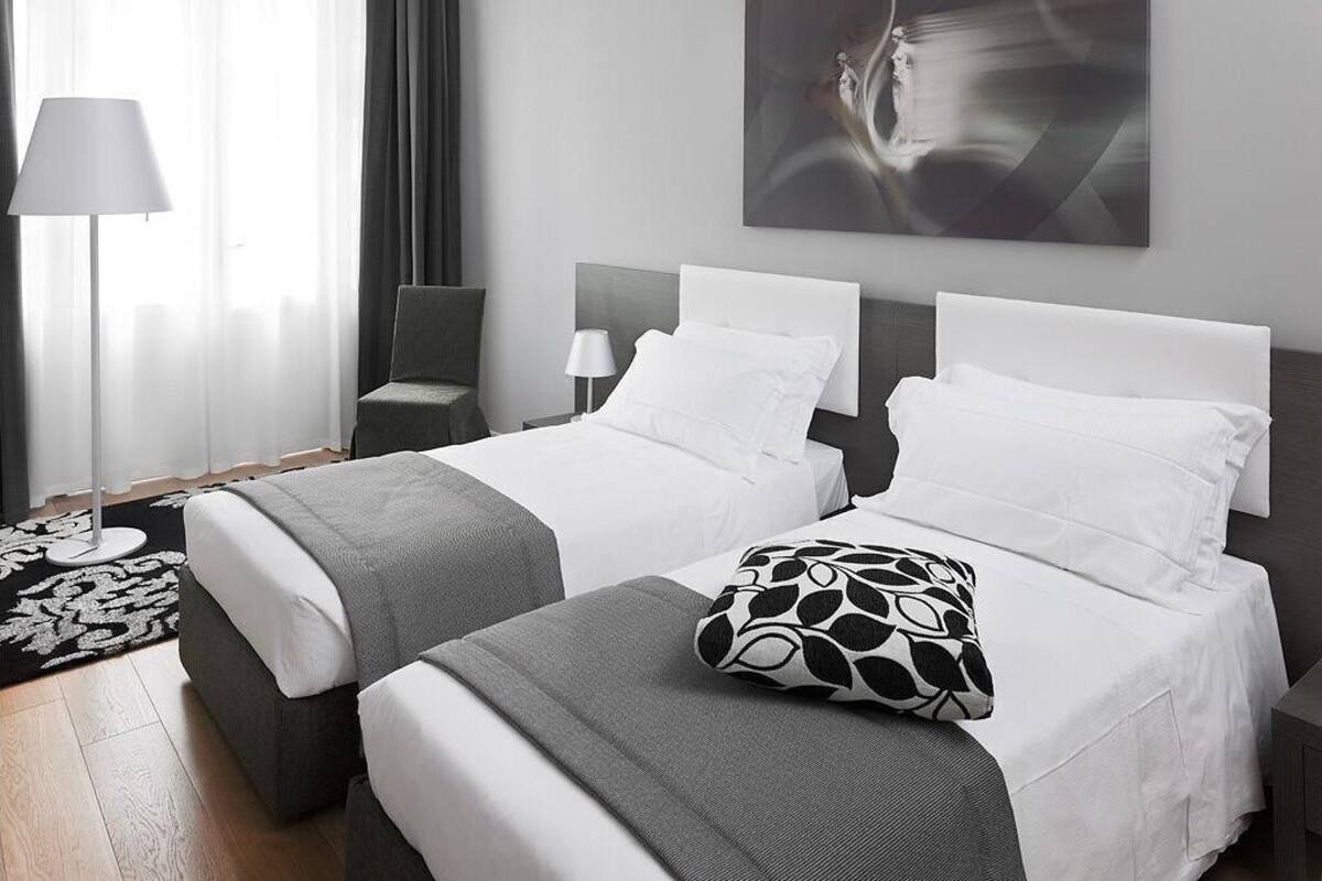 A hotel room with two beds, a large abstract painting, a lamp, and a patterned rug.