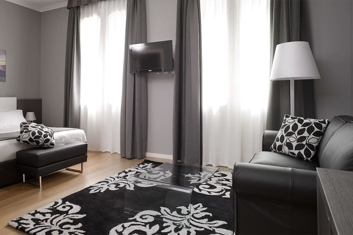 A modern hotel room with a bed, sofa, TV, and a lamp.
