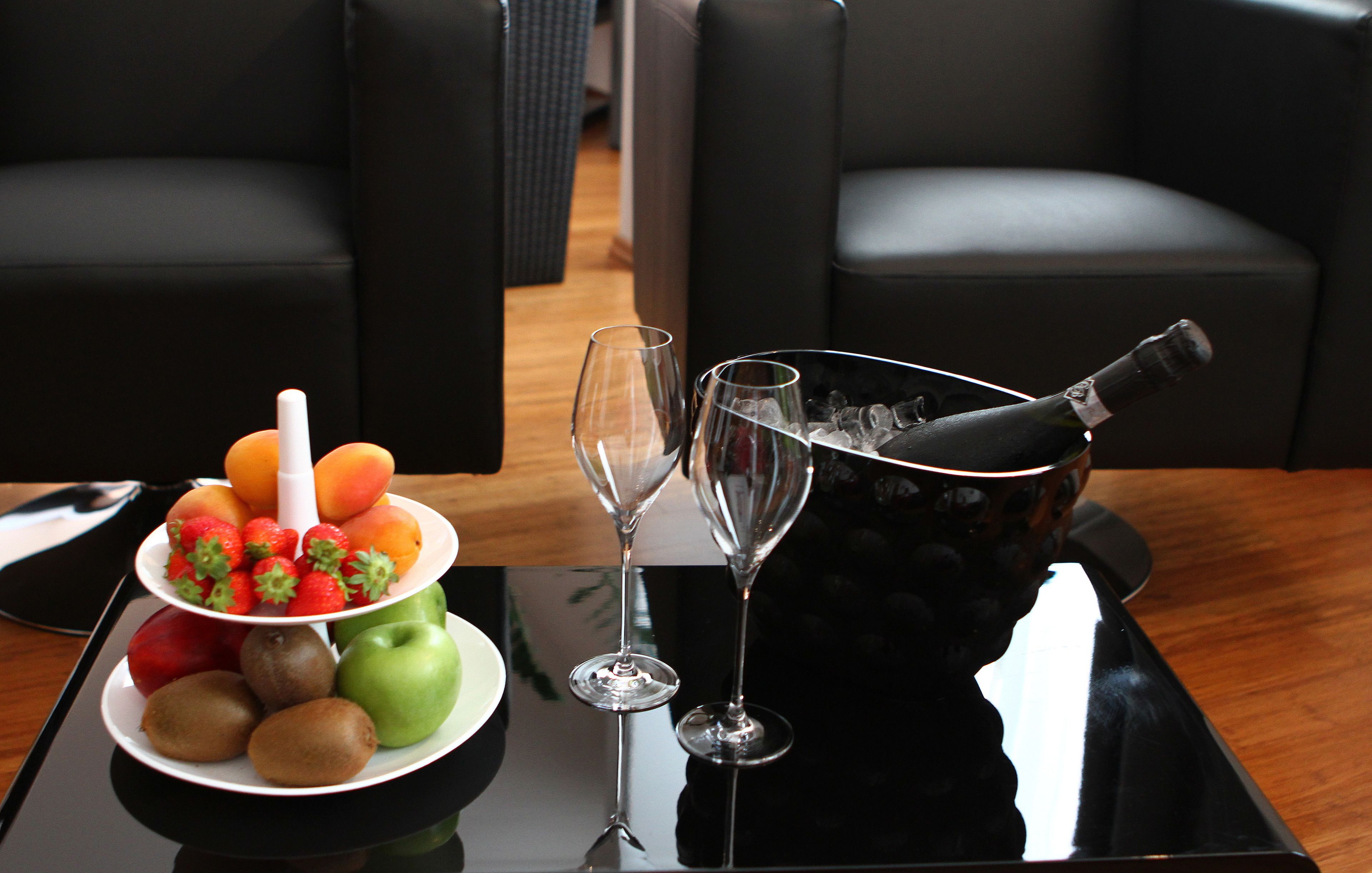 A table with a fruit platter, two wine glasses, and a bottle of champagne.