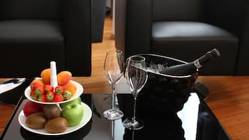 A table with a fruit platter, two wine glasses, and a bottle of champagne.