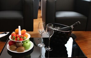 A table with a fruit platter, two wine glasses, and a bottle of champagne.