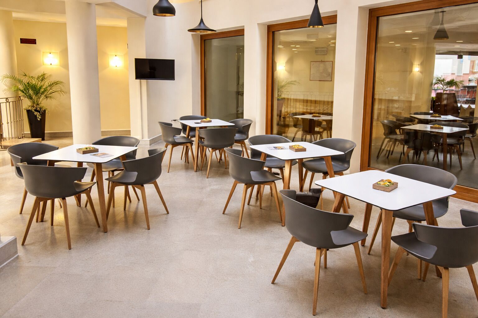 A modern dining area with tables and chairs, a TV on the wall, and a potted plant.