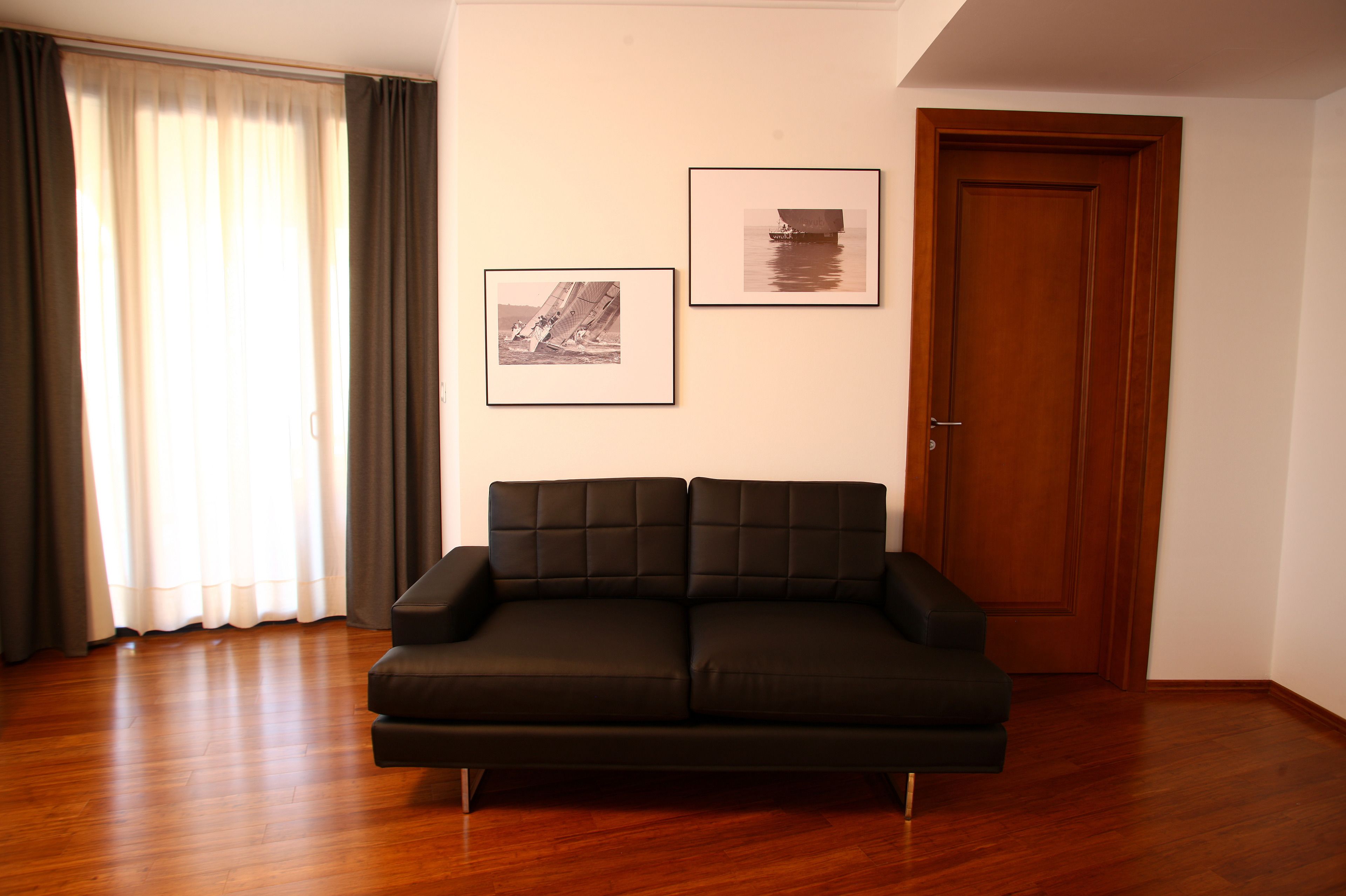 Ein Wohnzimmer mit einer schwarzen Couch, Holzböden, einer Tür und zwei gerahmten Bildern an der Wand.