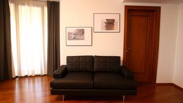 Ein Wohnzimmer mit einer schwarzen Couch, Holzböden, einer Tür und zwei gerahmten Bildern an der Wand.