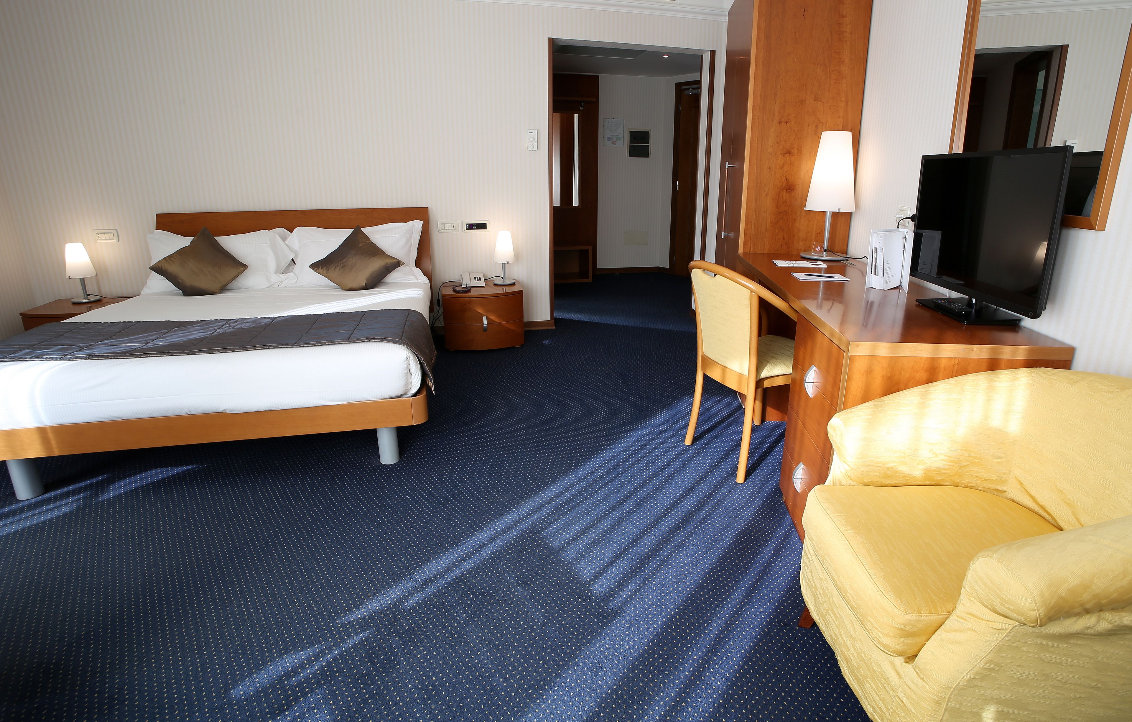 Ein Hotelzimmer mit Bett, Nachttischen, einem Schreibtisch mit Stuhl, einem Fernseher und einem Spiegel.