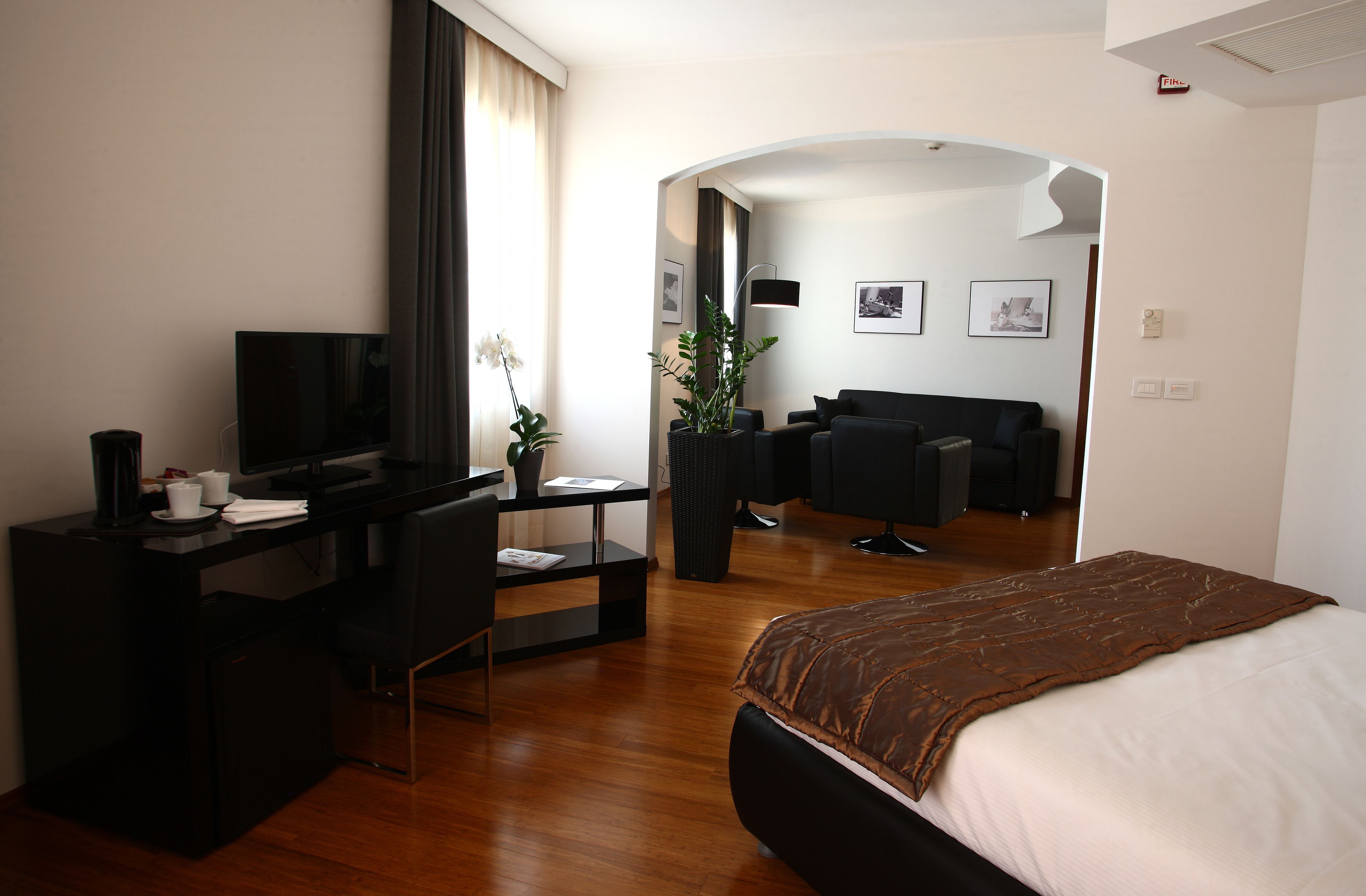 Habitación de hotel con cama, escritorio con computadora, televisor, sillón, planta en maceta y sofá.