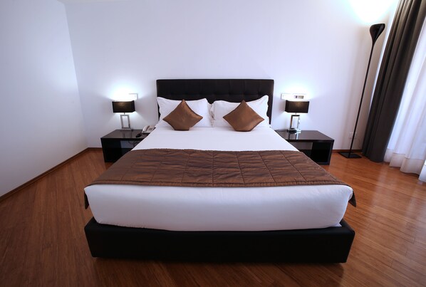 A neatly made bed with a black headboard, two bedside tables with lamps, and a wooden floor.