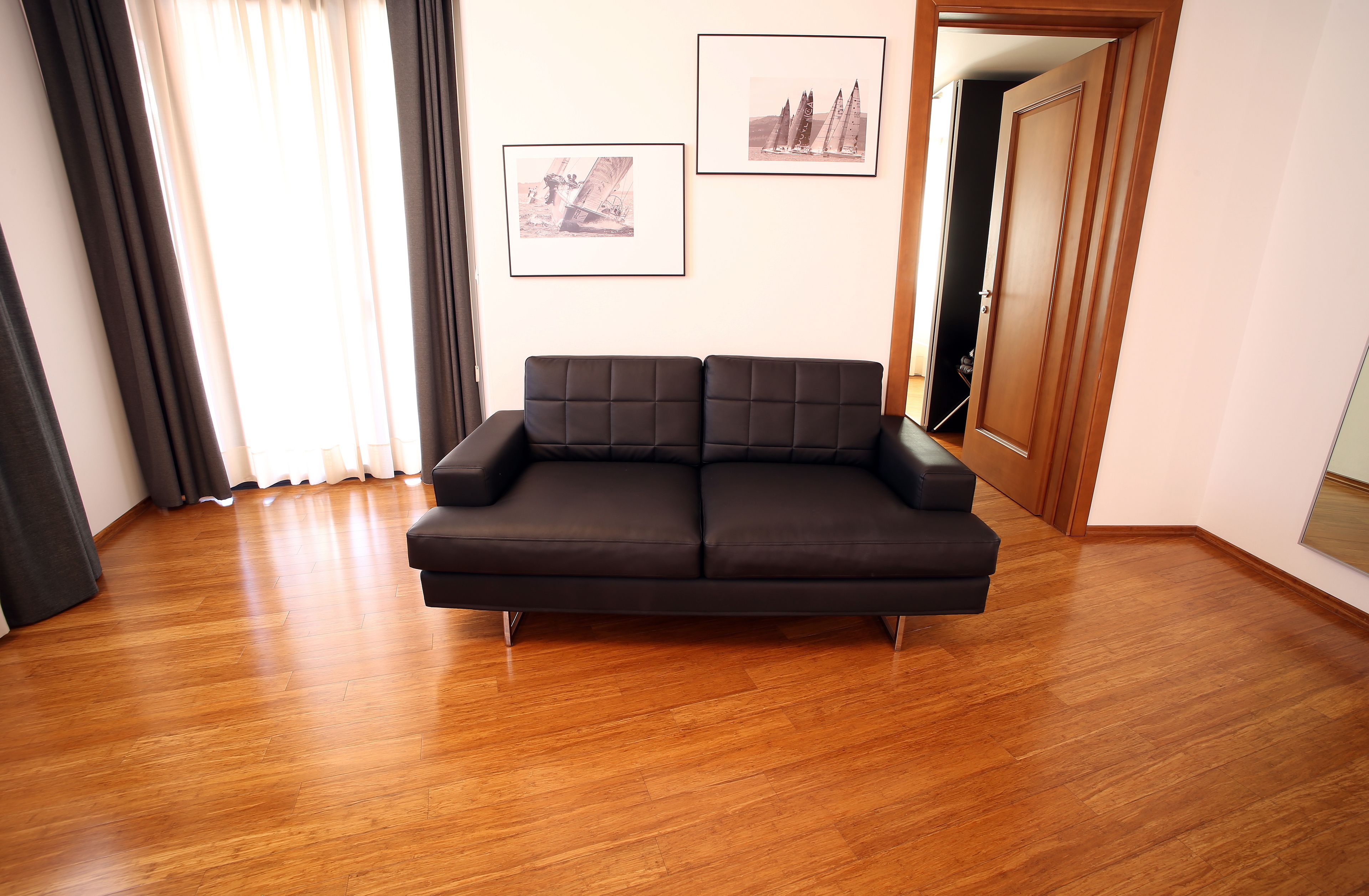 Una sala de estar moderna con un sofá oscuro, piso de madera y dos cuadros en la pared.