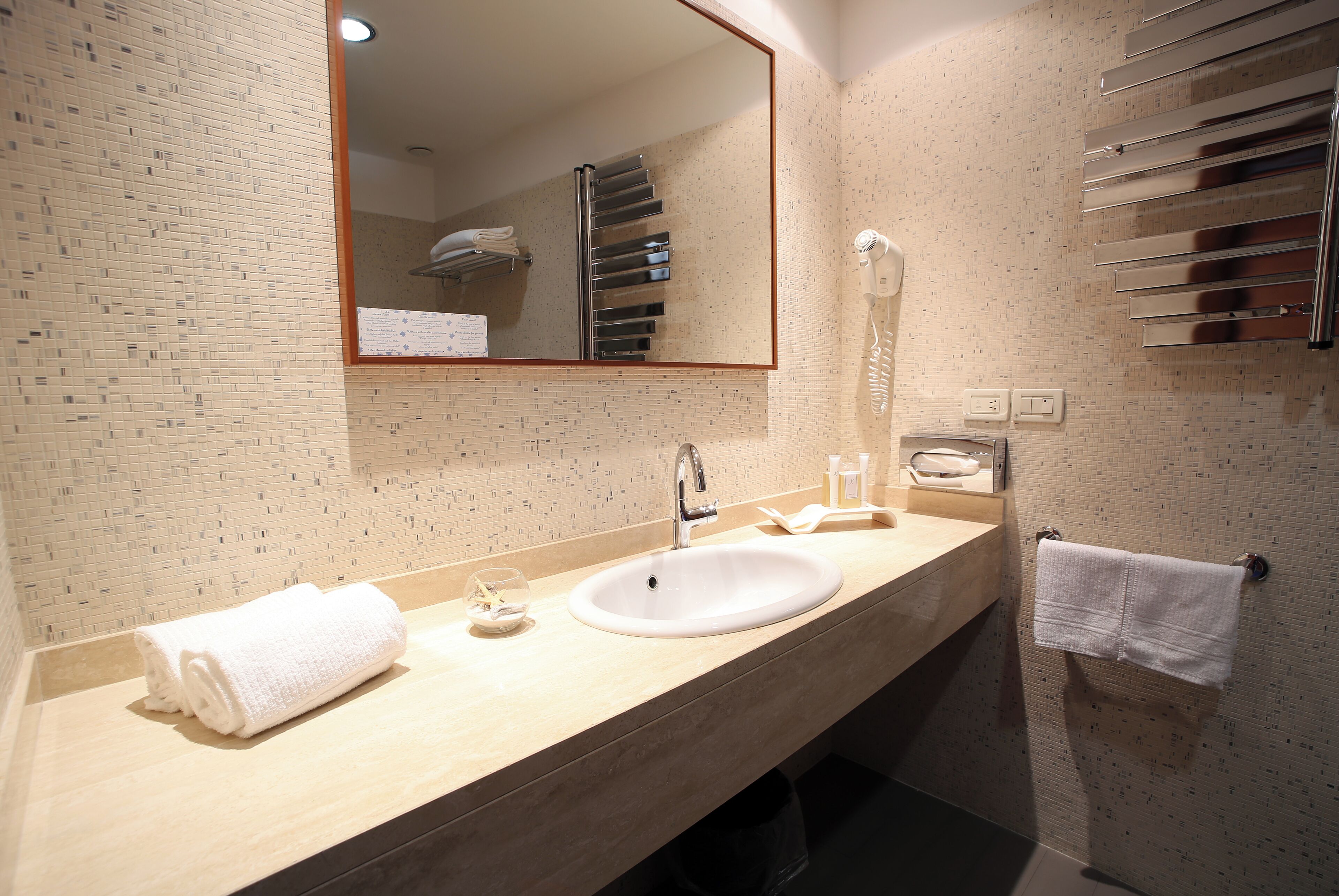 A bathroom with a sink, mirror, towel rack, and a wall-mounted hairdryer.