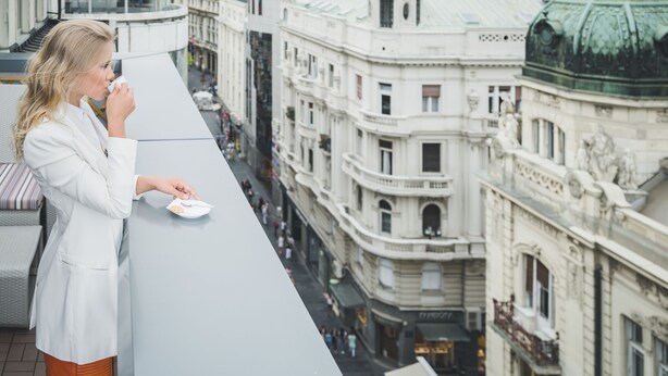 A person in a white coat standing on a balcony overlooking a cityscape with historic buildings. - Belgrade Art Hotel, a member of Radisson Individuals (Belgrade)