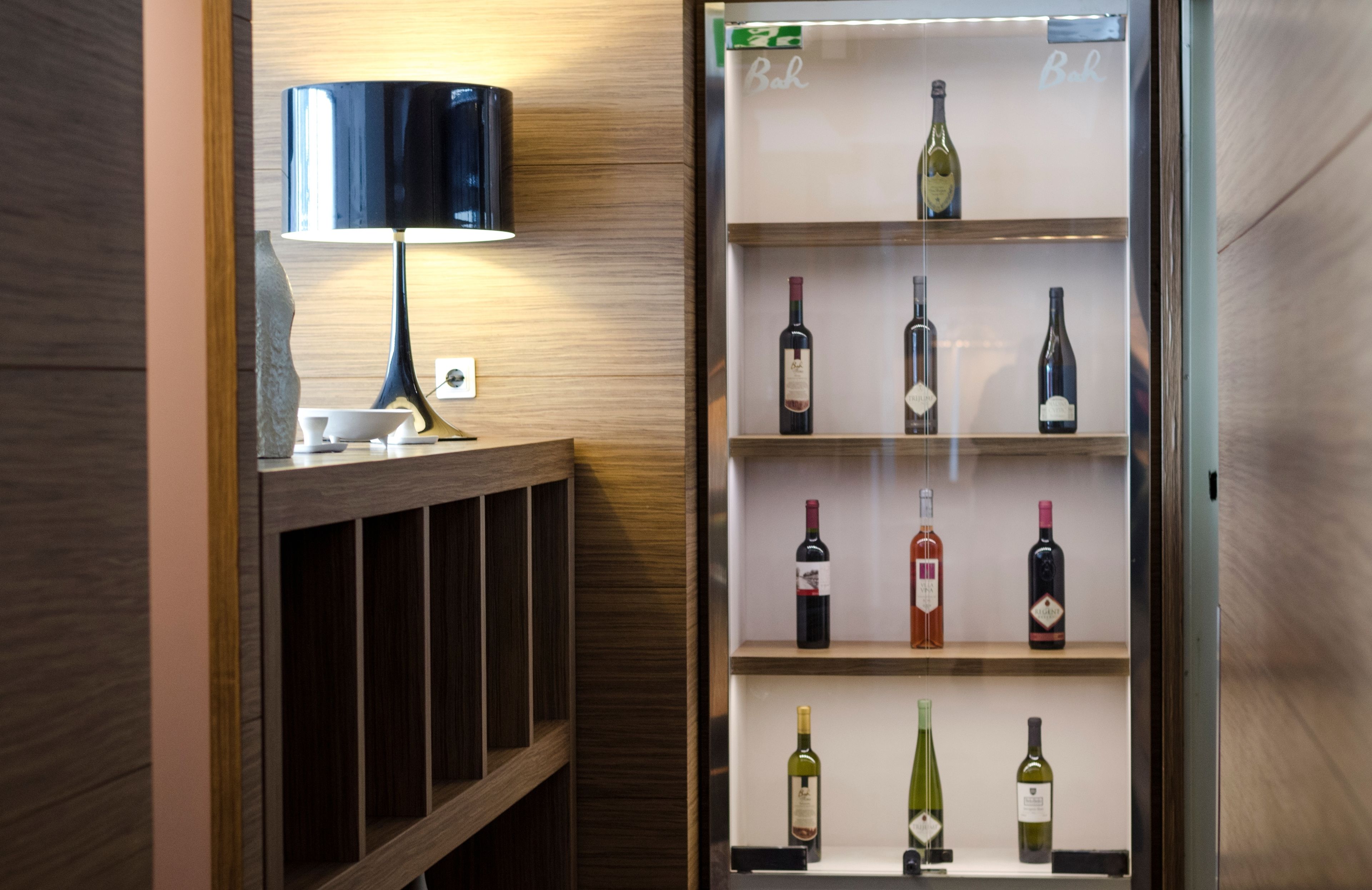 A minibar with a lamp and a wine refrigerator stocked with various bottles.