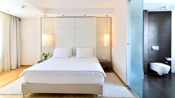 A modern hotel room with a large bed, a glass shower enclosure, and a separate bathroom.