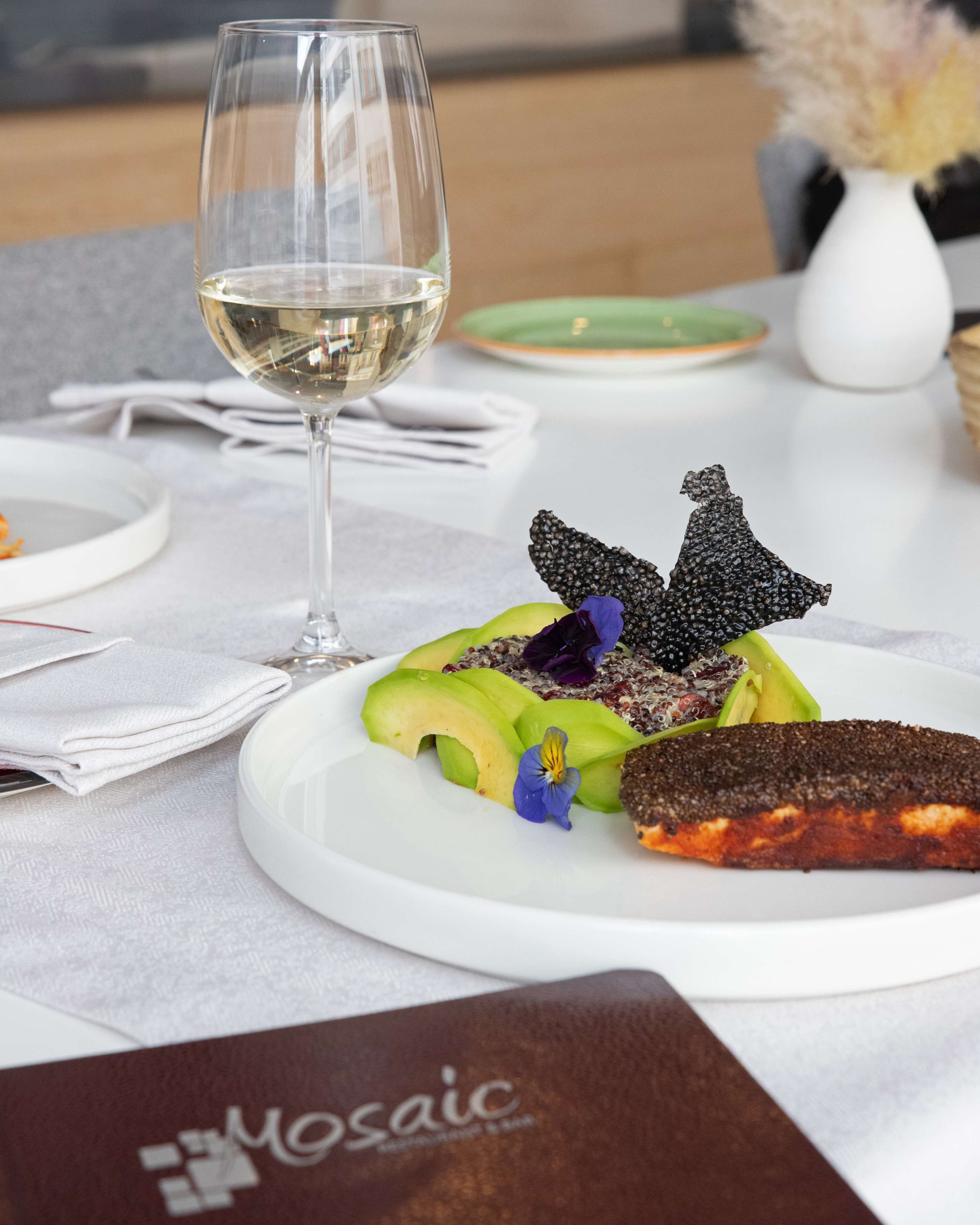 Una mesa de comedor con un plato de comida blanco, una copa de vino blanco y un menú.