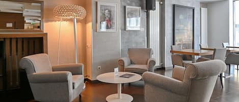 A modern lounge area with grey upholstered armchairs, a round white table, and a floor lamp.