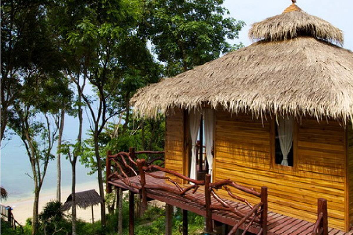 Una cabaña de madera con techo de paja, terraza de madera y vista a la playa.