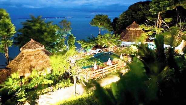 Un resort tropical con cabañas de techo de paja, piscina y exuberante follaje.