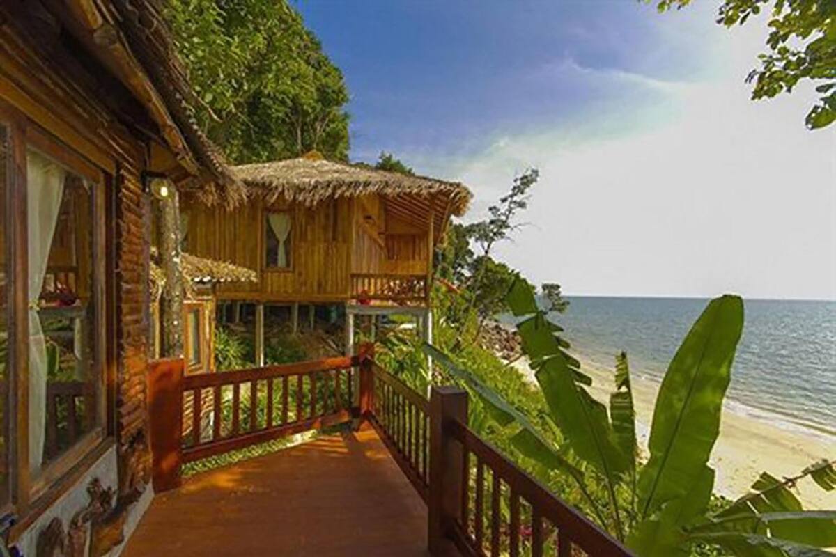 Una casa de madera con techo de paja, un balcón y vista a la playa.