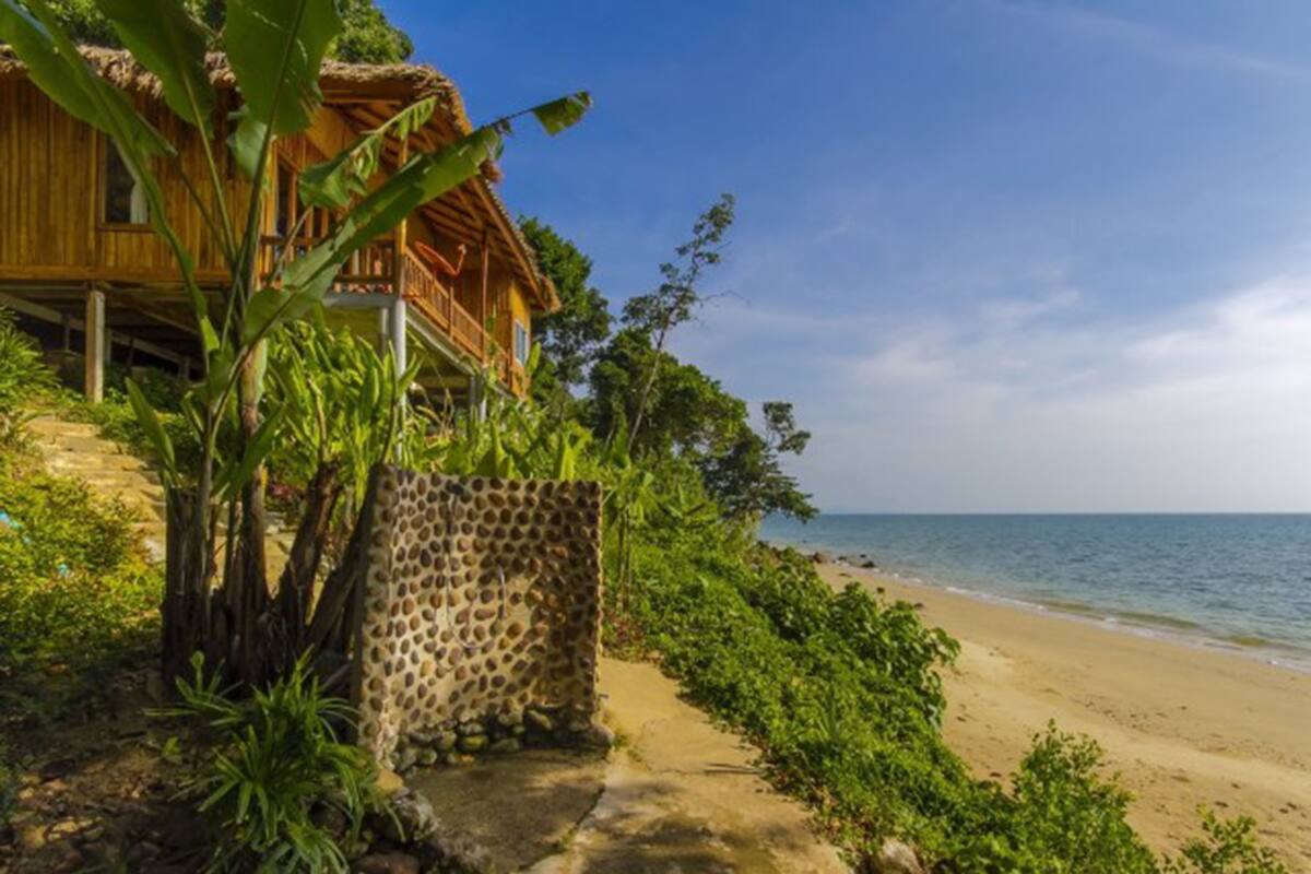 Una casa de madera con techo de paja, un camino de hormigón y vistas a la playa.