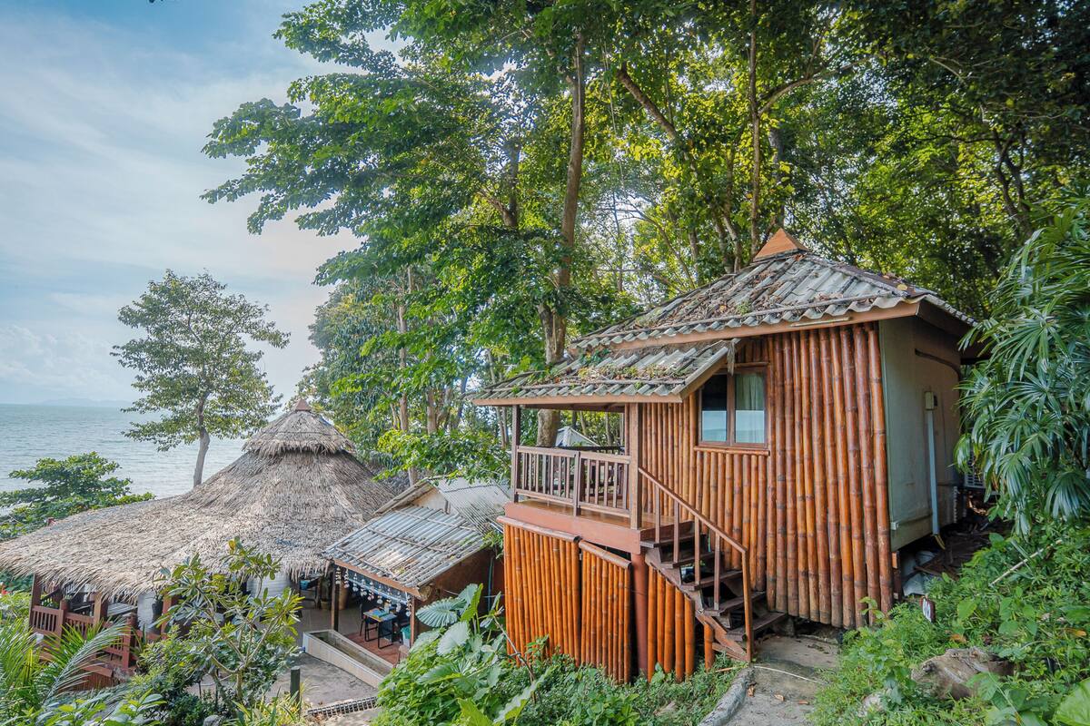 Una casa de bambú con balcón, techo de paja y vista al mar.