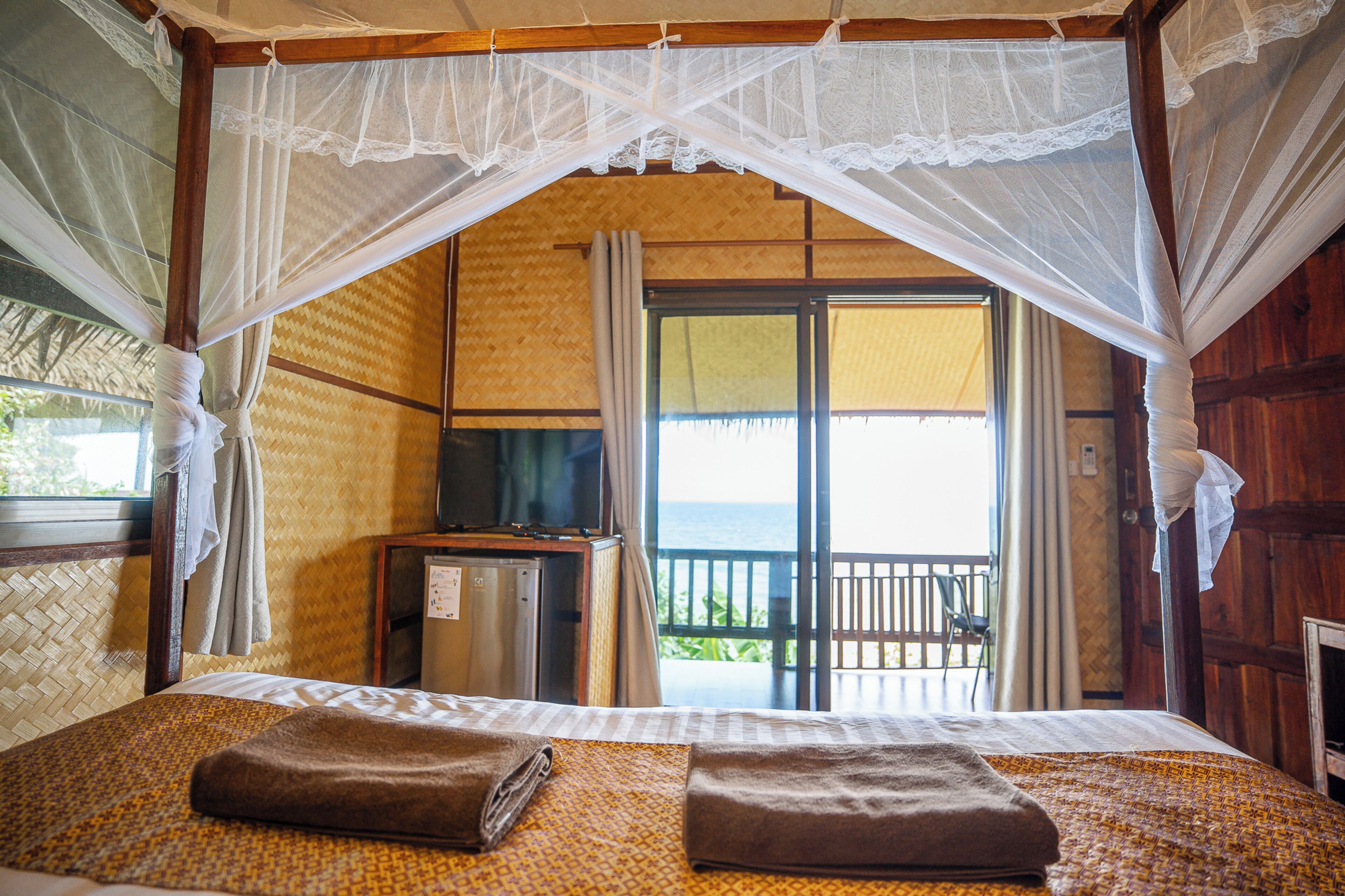 A room with a bed, a TV, and a balcony with a view of the ocean.
