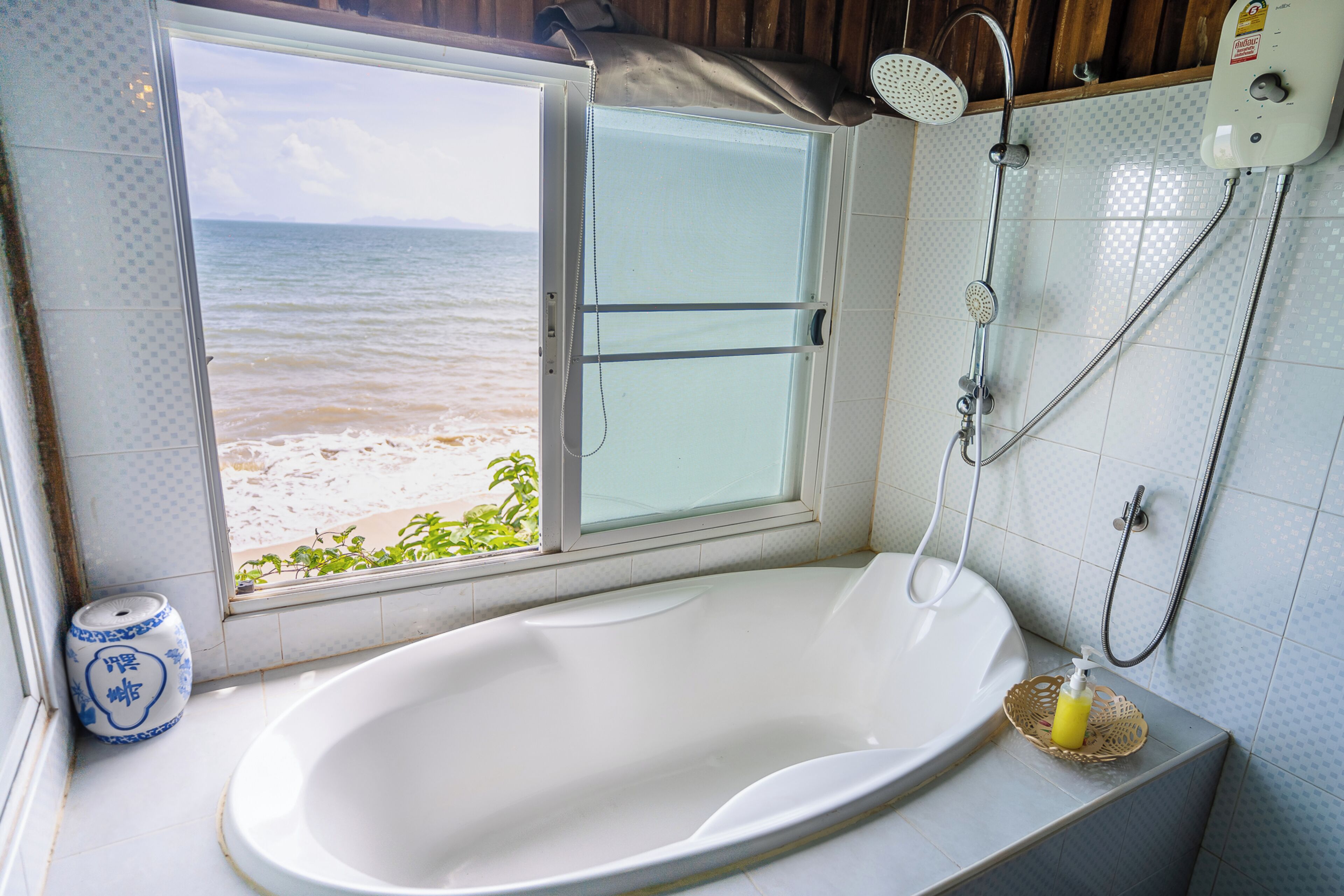 Casa de banho com banheira, chuveiro e janela com vista para uma praia.