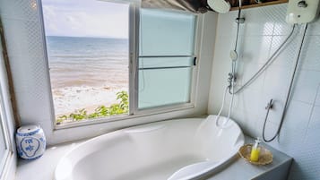 Casa de banho com banheira, chuveiro e janela com vista para uma praia.