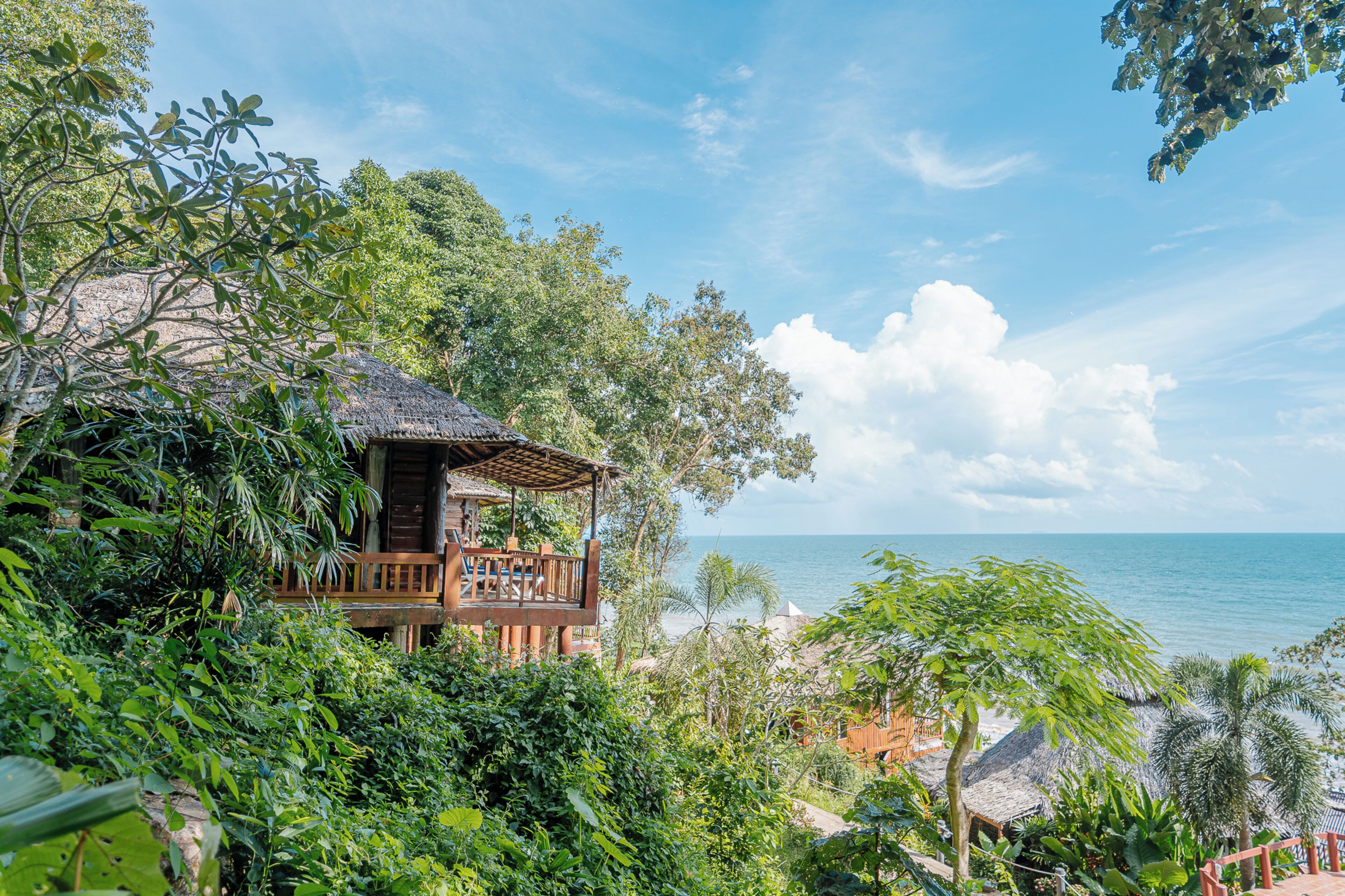 A wooden structure with a balcony overlooking a beach, surrounded by lush greenery.