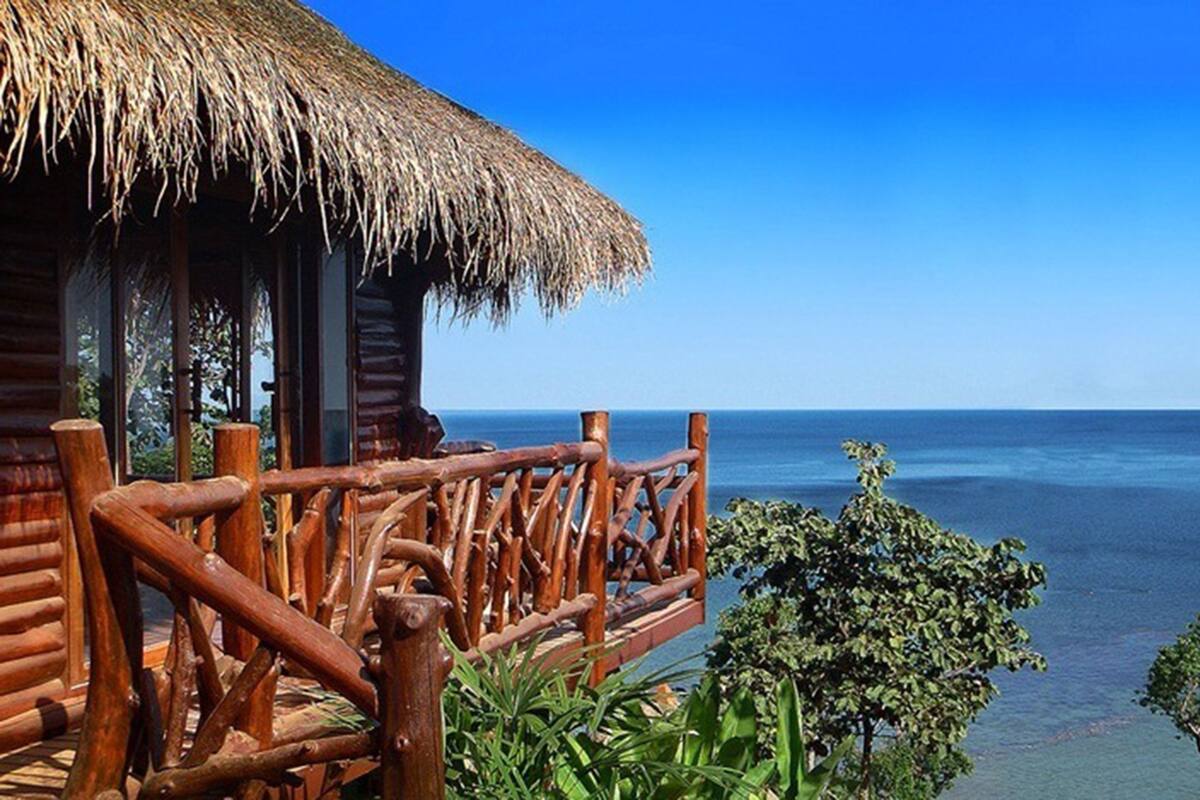 Una cabaña de madera con techo de paja que domina un mar tranquilo.