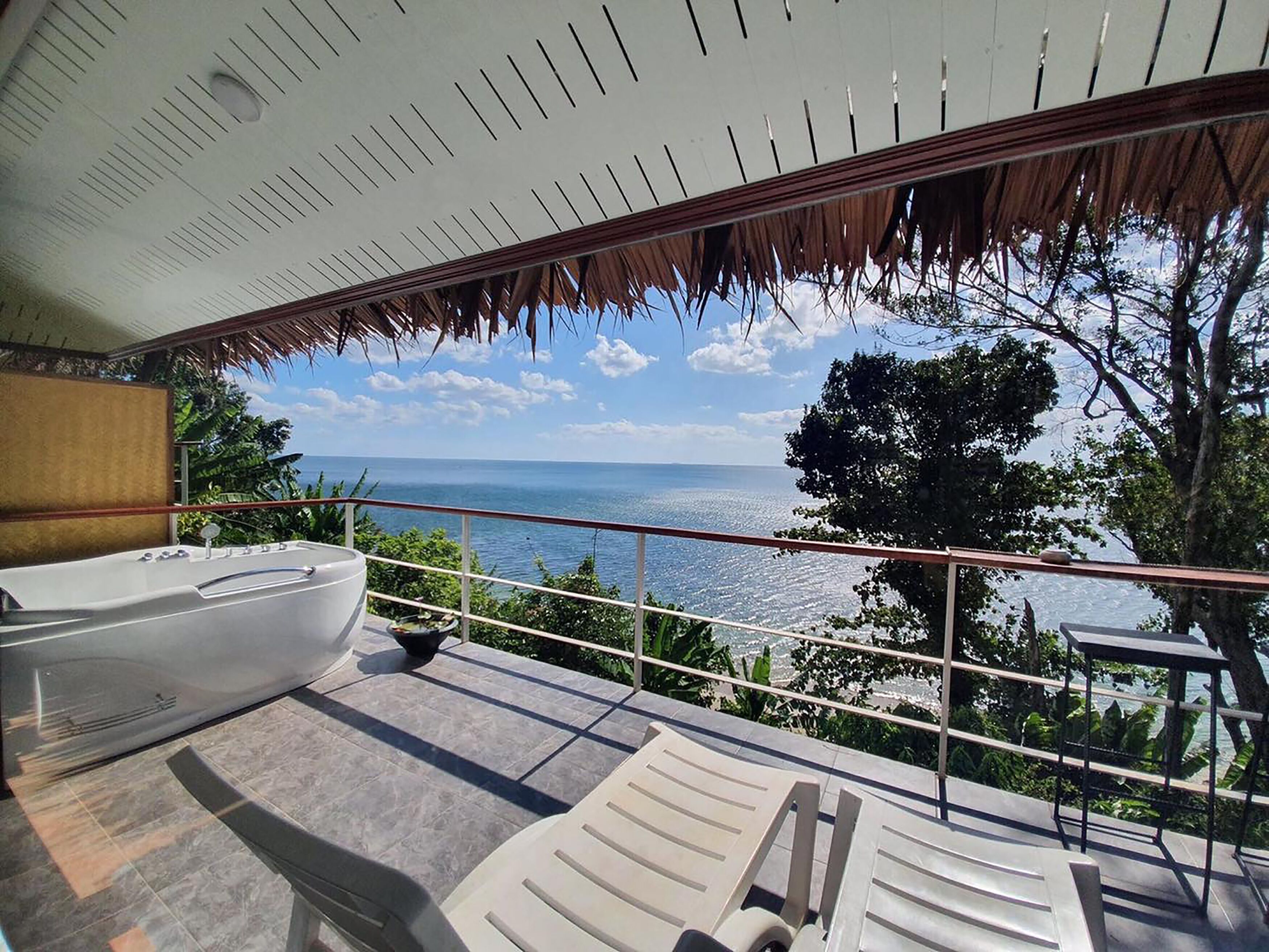 Ein Balkon mit Meerblick, einer Badewanne und Liegestühlen.