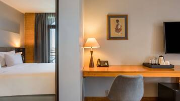 Una habitación de hotel con una cama, un escritorio con lámpara, una silla, un cuadro enmarcado, un televisor y una cafetera.