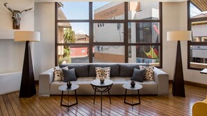 A modern living room with a sofa, two small tables, and a large window with a view of buildings and a street. - Radisson Hotel Tamboho Waterfront Antananarivo (Antananarivo)