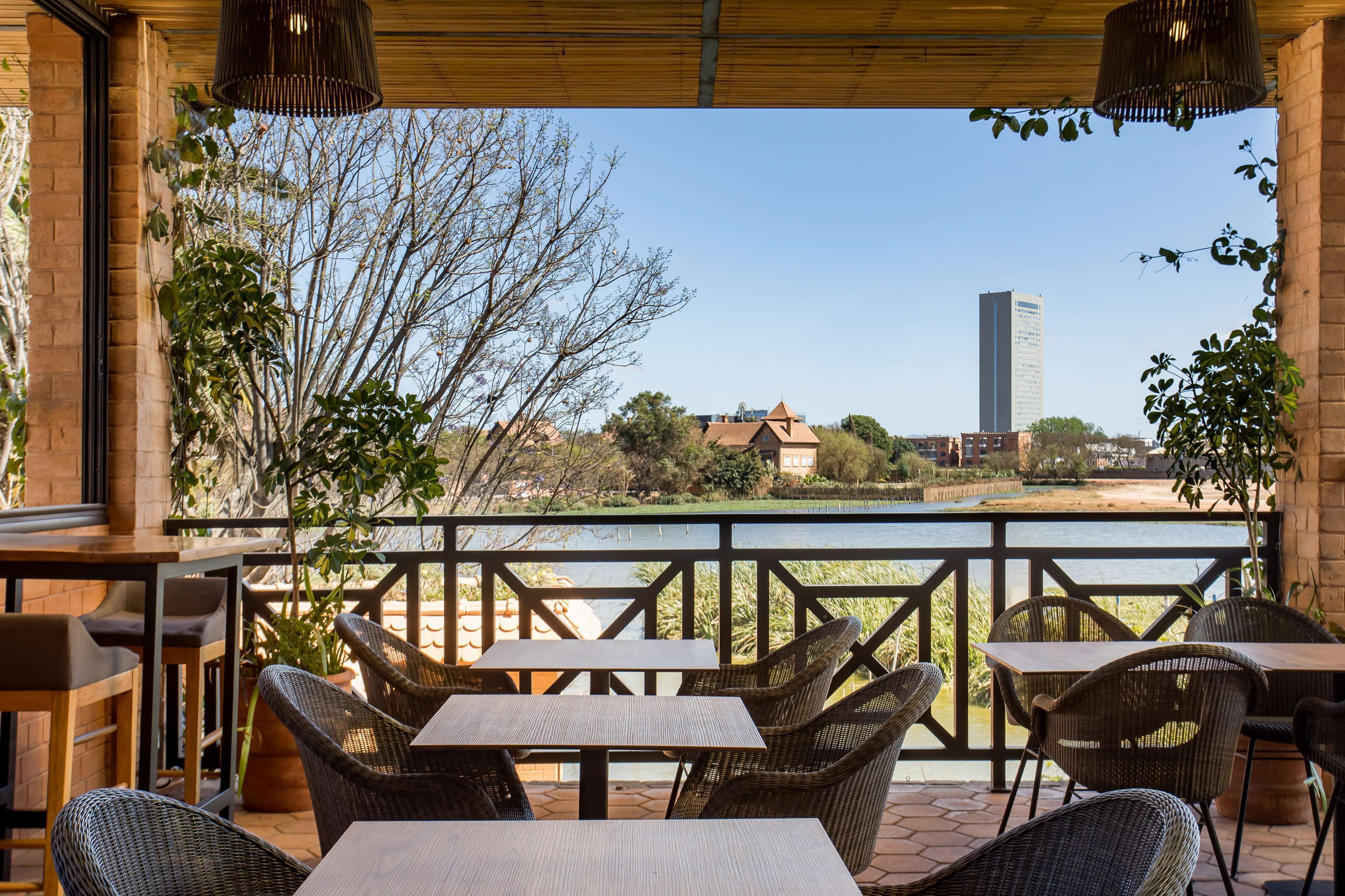 Een terras buiten met rieten meubilair en uitzicht op een rivier en gebouwen op de achtergrond.