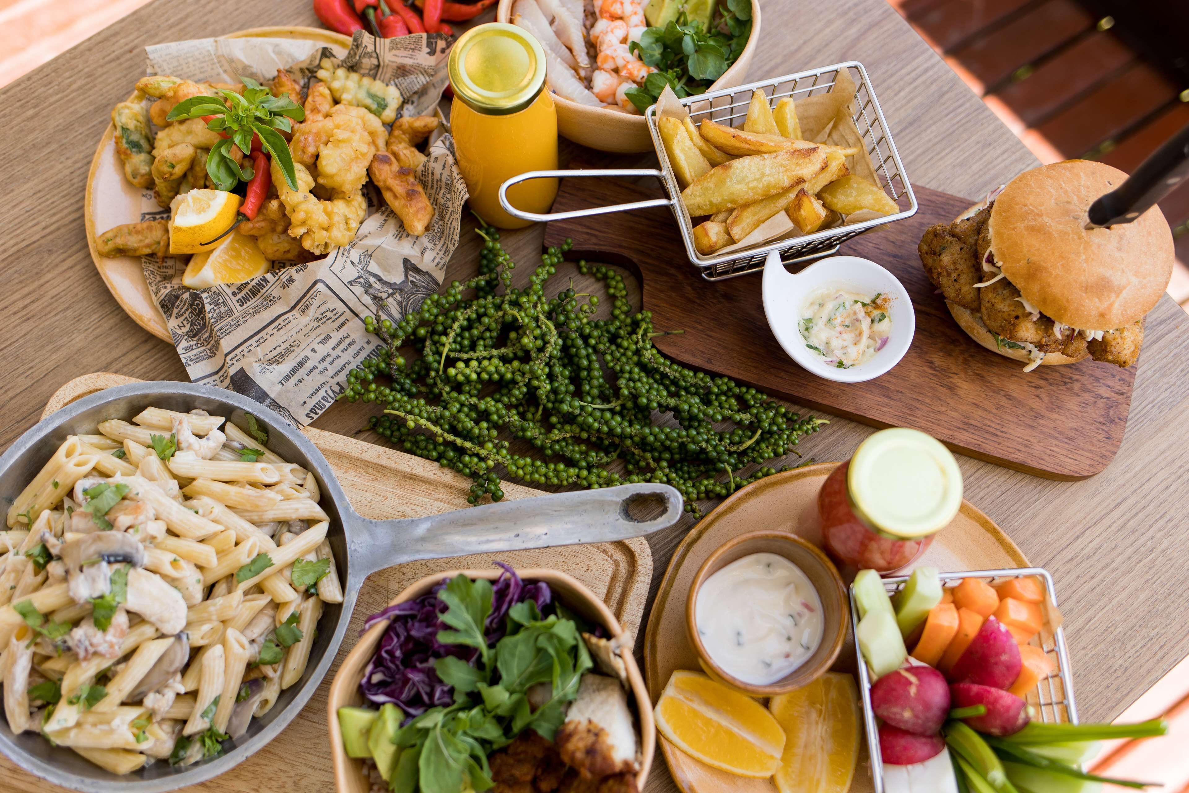 Verschiedene Gerichte, darunter Pasta, frittierte Calamare und ein Burger, begleitet von Beilagen wie Pommes und Salat.