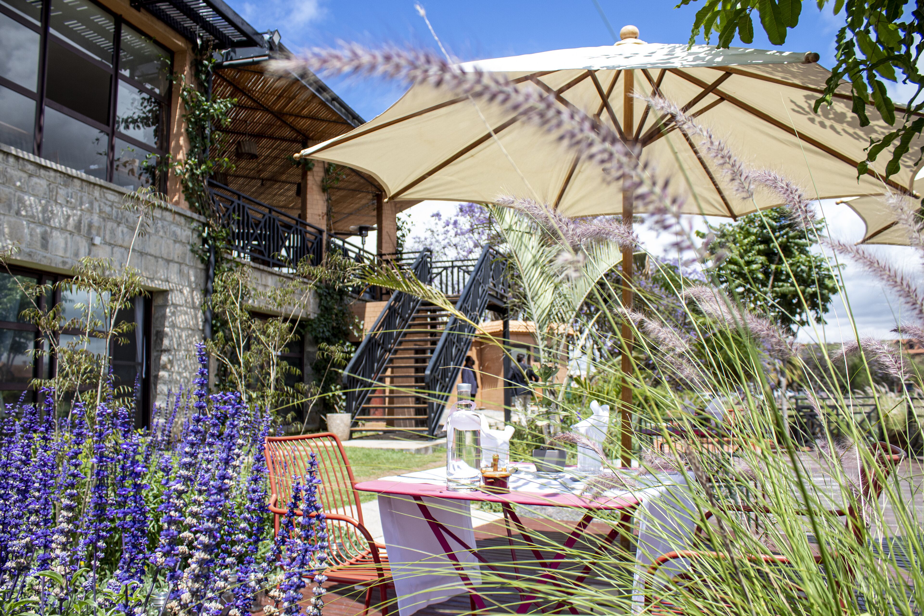 An outdoor patio with a table and chairs, surrounded by purple flowers and a large umbrella.