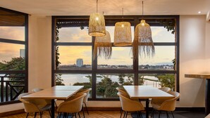 A dining area with a large window, wicker chairs, a wooden table, and hanging rattan lamps. - Radisson Hotel Tamboho Waterfront Antananarivo (Antananarivo)