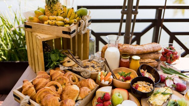 A breakfast buffet with fruits, pastries, and beverages on a wooden table by a lakeside. - Radisson Hotel Tamboho Waterfront Antananarivo (Antananarivo)
