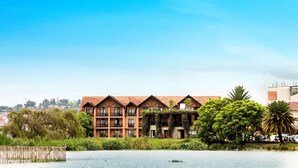 A hotel with multiple floors, balconies, and a garden area with trees and a water body. - Radisson Hotel Tamboho Waterfront Antananarivo (Antananarivo)