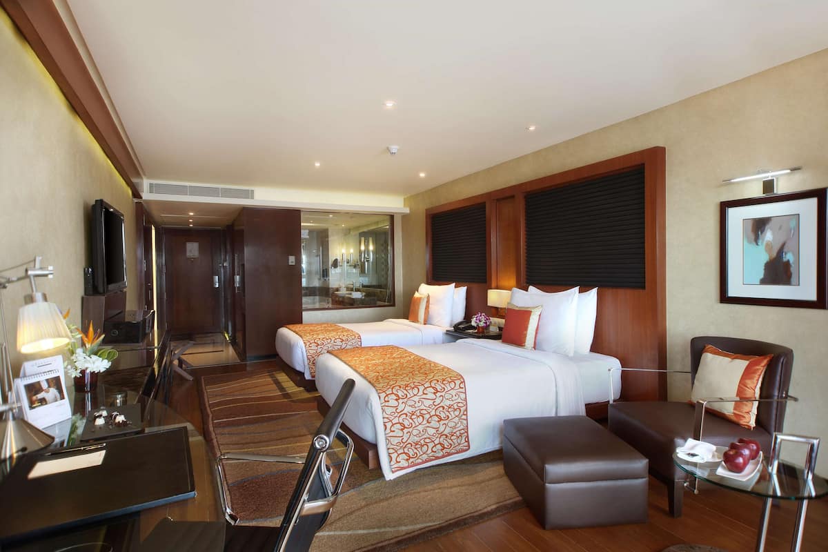 A hotel room with two beds, a desk, a chair, a sofa, and a small table with a fruit plate.