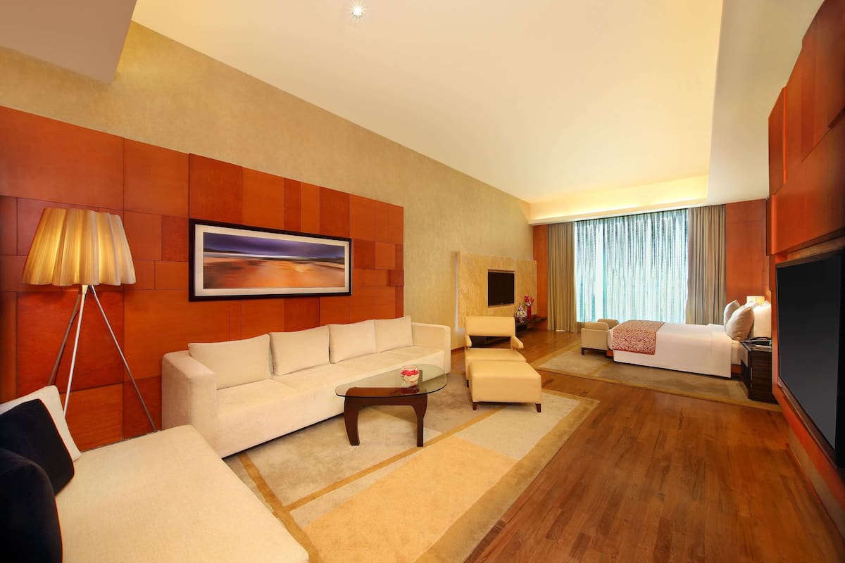 A modern hotel room with a sofa, armchair, and a flat-screen TV.