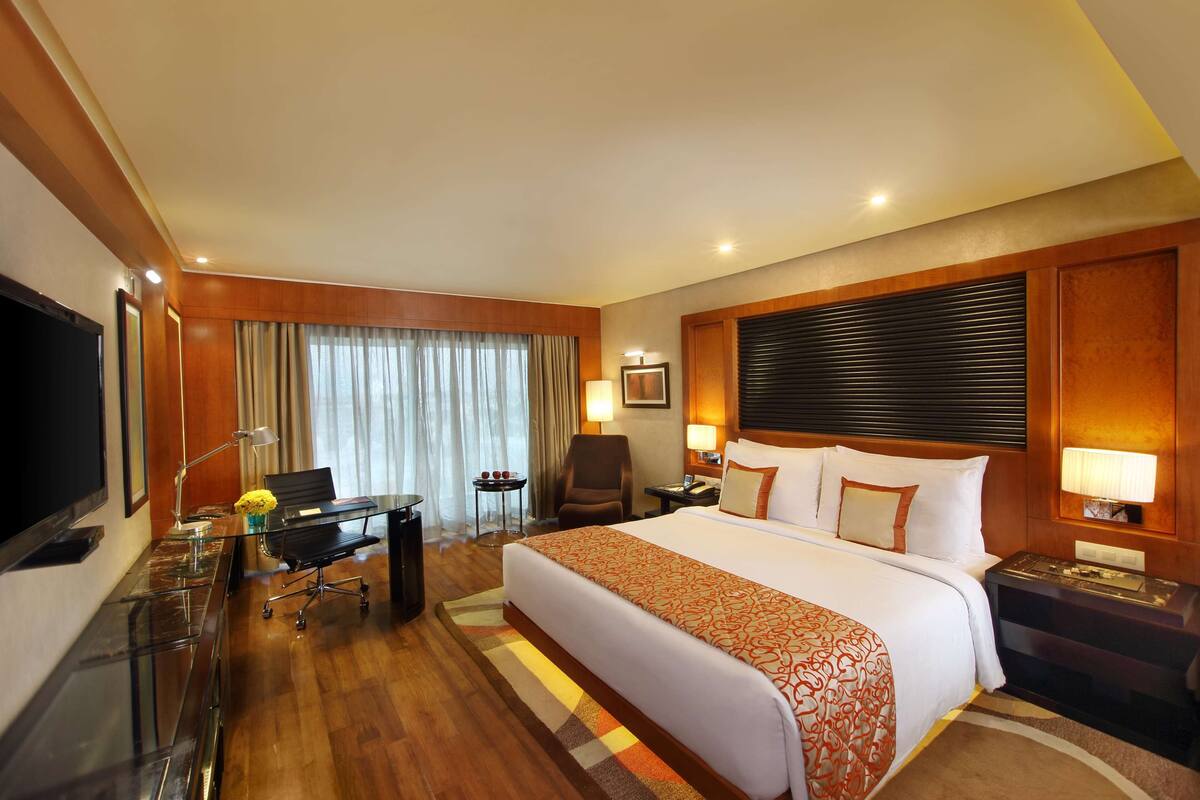A hotel room with a large bed, a desk with a chair, a TV, and a lamp.